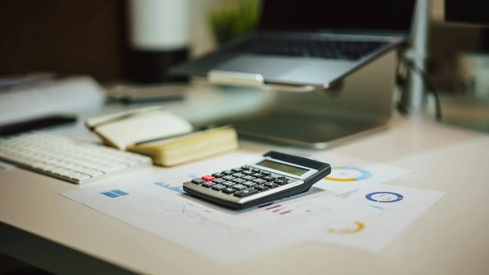 Calculadora sobre documentos con gráficas junto a una laptop en un escritorio
