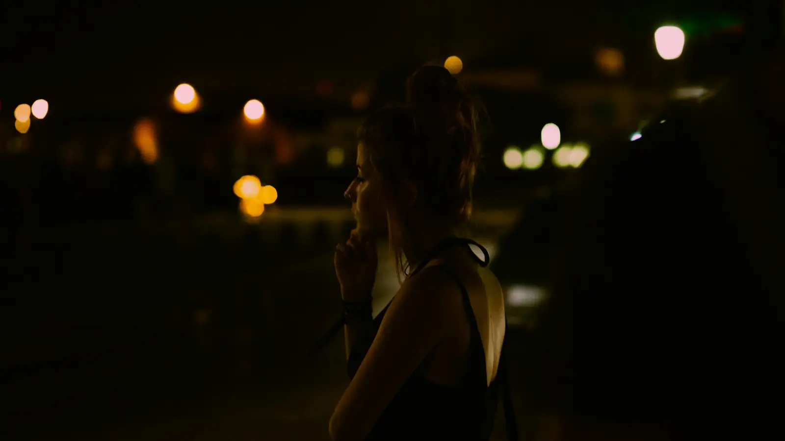 Mujer pensativa de noche con luces de la ciudad desenfocadas al fondo